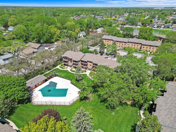 Aerial view of residential buildings surrounded by greenery and a swimming pool in the courtyard.