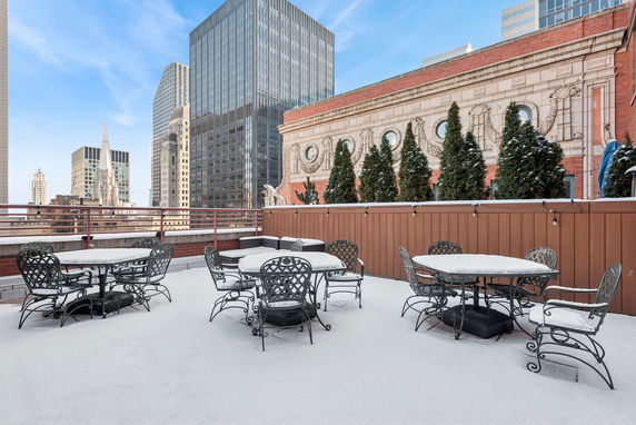 Rooftop with tables and chairs, surrounded by tall buildings.