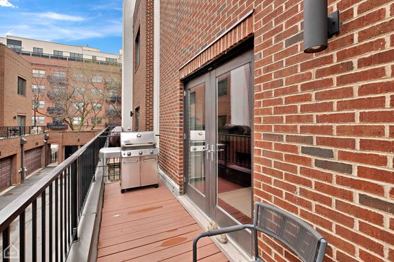 Balcony view of a brick building with a grill and outdoor seating.