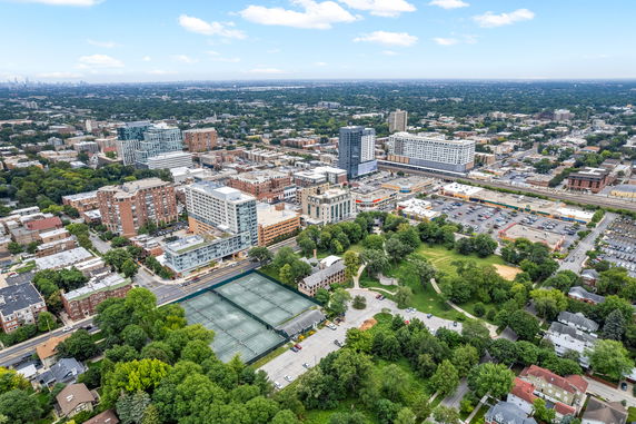 Panoramic aerial view of a city with buildings, green spaces, and tennis courts.