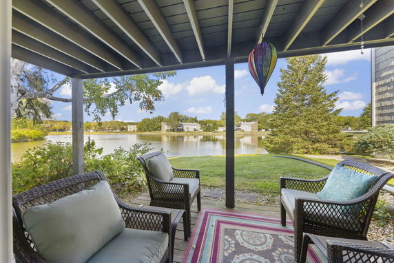 View from a covered patio overlooking a lake with houses and trees in the distance.