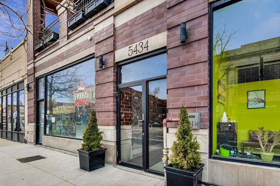 Front view of a commercial building with large windows and potted plants.