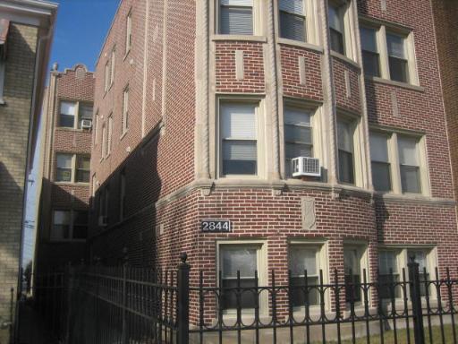 Front view of a multi-story brick apartment building with decorative stone trim and window air conditioning units.