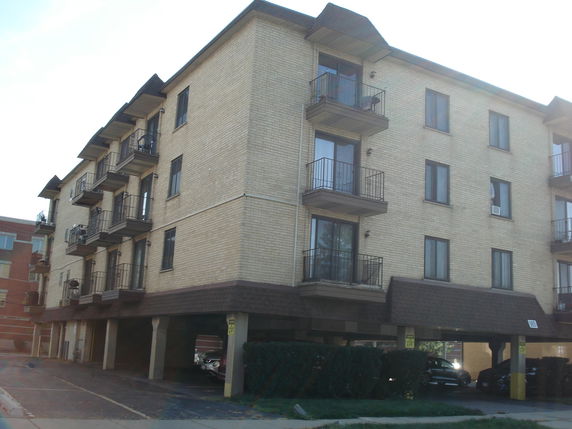 Front view of a multi-story apartment building with balconies and covered parking area.