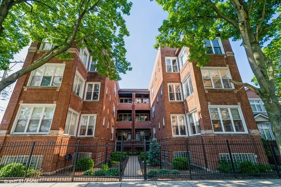 Front view of a multi-story brick apartment building with large windows and a gated entrance.