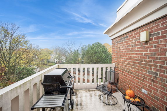 View from a balcony with a grill and seating area overlooking trees and houses.