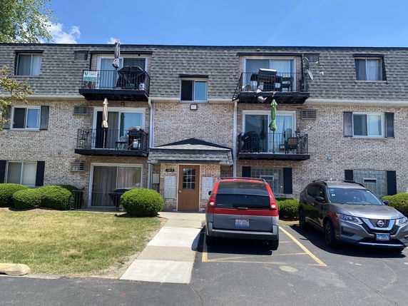 Front view of a three-story apartment building with balconies and parked cars in front.