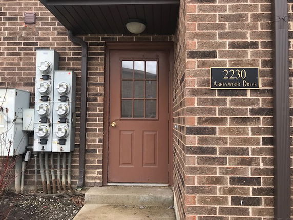 Front view of a brick building with a brown door and a sign reading '2230 Abbeywood Drive'.