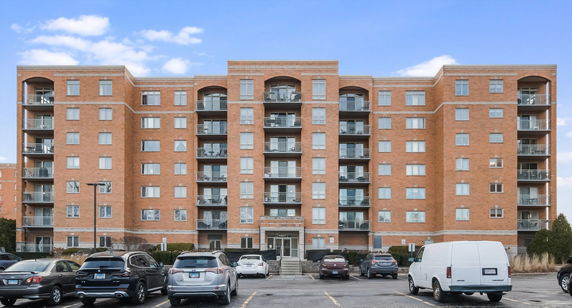 Front view of a multi-story brick building with balconies and a parking area in front.