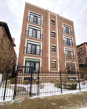 Front view of a multi-story brick building with multiple windows and a gated entrance.