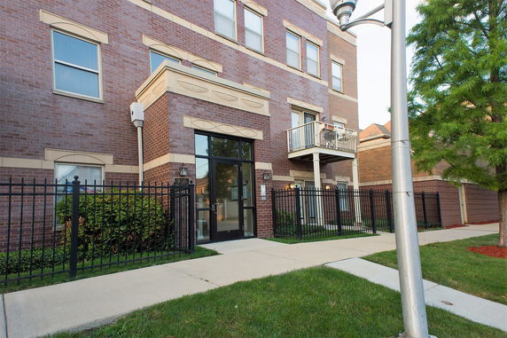 Front view of a multi-story brick building with balconies and a gated entrance.