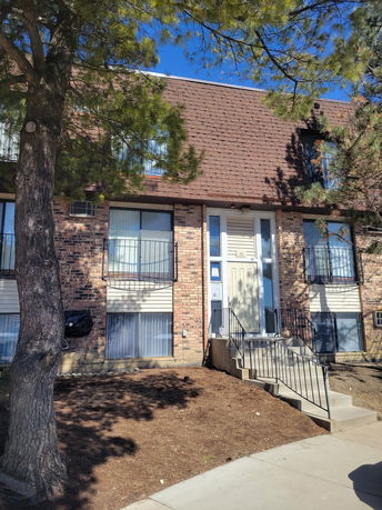 Front view of a two-story brick building with a brown shingled roof and steps leading to the entrance.