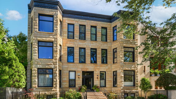 Front view of a three-story house with stone facade and large windows.