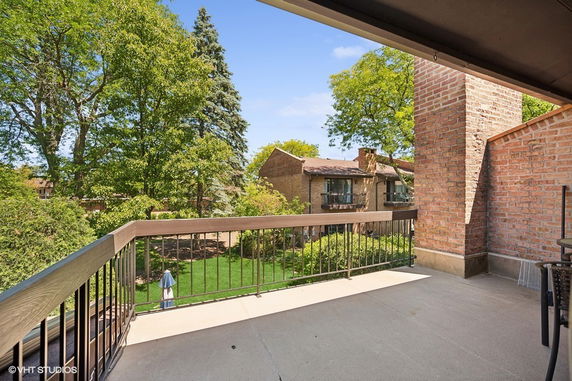 Balcony view overlooking a garden and neighboring brick buildings.