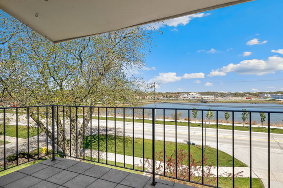 View from a balcony overlooking a road, river, and distant buildings under a clear blue sky.