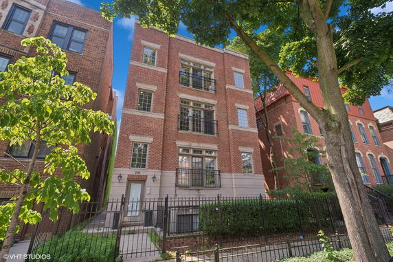 Front view of a multi-story brick building with iron balconies and a gated entrance.