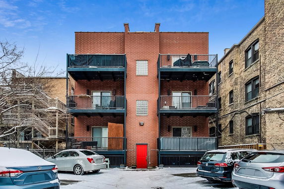Front view of a multi-story brick building with balconies and a red door.