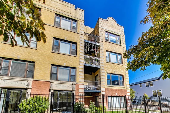 Front view of a multi-story brick apartment building with balconies and metal fencing.