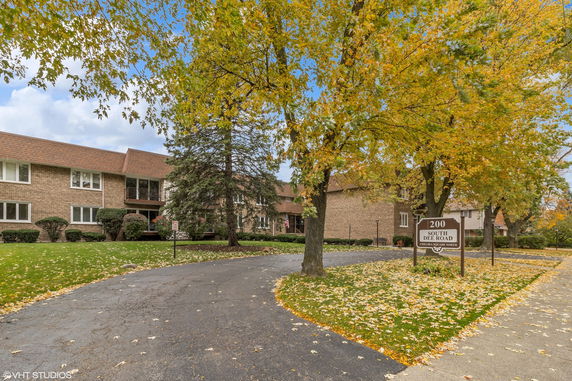 Front view of a two-story brick building with a peaked roof and surrounding autumn trees.