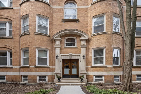 Front view of a brick apartment building with curved bay windows and an arched entrance.