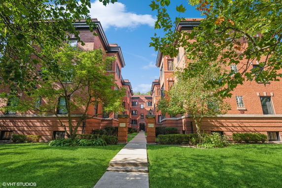 Front view of a brick apartment building with multiple floors and entrance pathway.