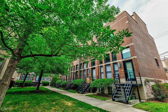 Front view of a multi-story brick building with exterior stairs and greenery.