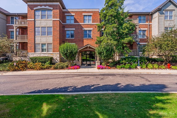 Front view of a multi-story brick building with balconies and a landscaped entrance.