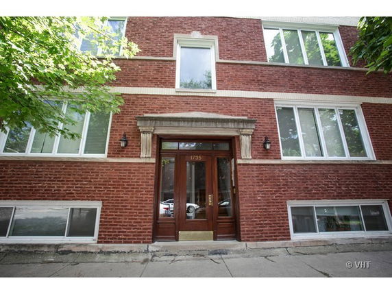 Front view of a brick apartment building with large windows and a wooden entrance door.