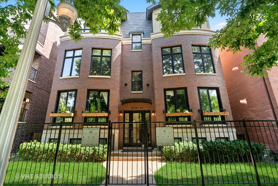 Front view of a multi-story brick building with large windows and a fenced entrance.