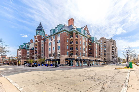 Front view of a multi-story building with a corner tower and retail shops at street level.