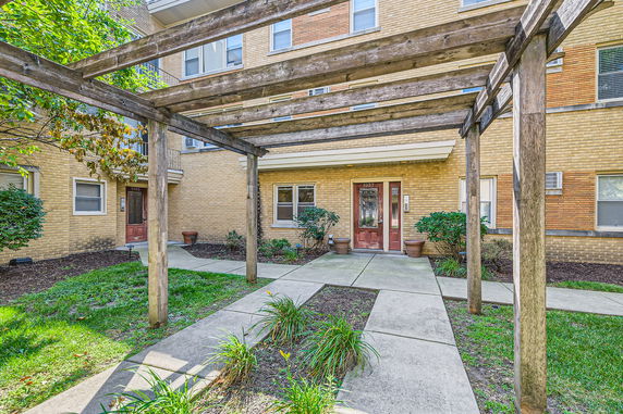 Front view of a brick multi-story residential building with a wooden pergola at the entrance.