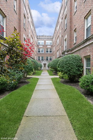 Front view of a brick apartment building with a pathway and landscaped shrubs.