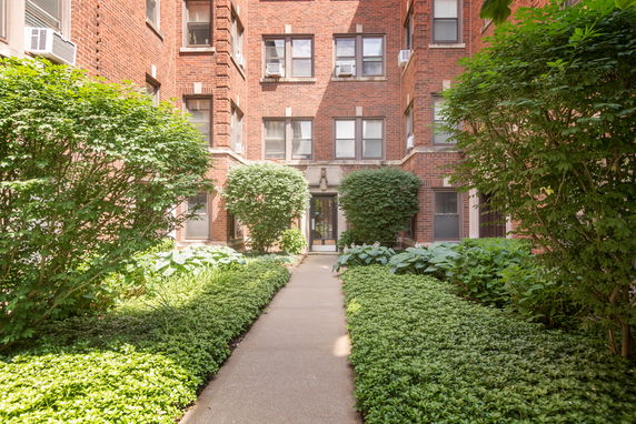 Front view of a brick apartment building with pathway and greenery.