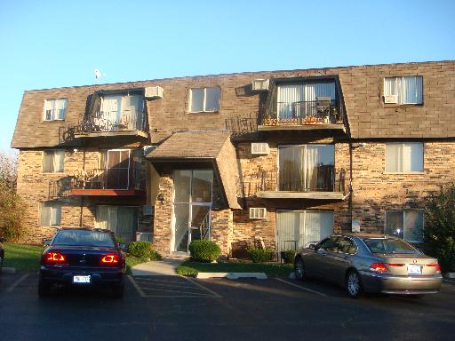 Front view of a multi-story apartment building with balconies and parking area in front.