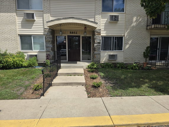 Front view of a multi-story apartment building with entrance stairs and surrounding greenery.