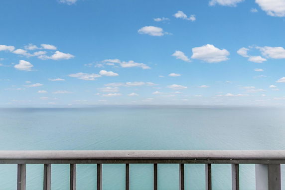 Wide angle view of the ocean with a clear blue sky, seen from behind a railing.