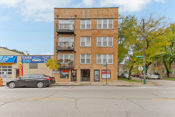 Front view of a four-story brick building with balconies and a commercial ground floor.