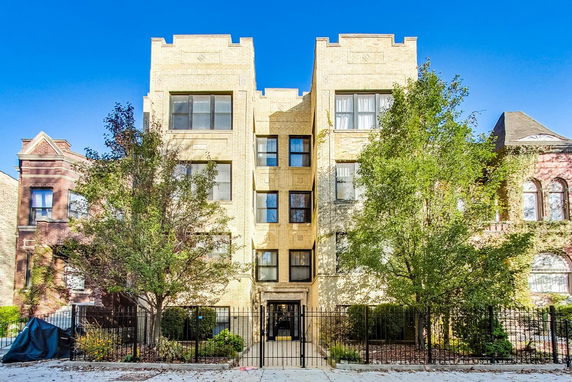 Front view of a multi-story brick building with large windows and a gated entrance.