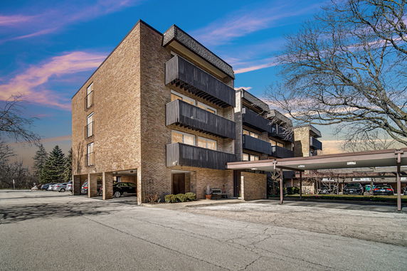 Front view of a multi-story brick building with balconies and covered parking area.