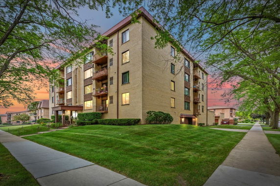 Front view of a multi-story apartment building with balconies and a landscaped lawn.