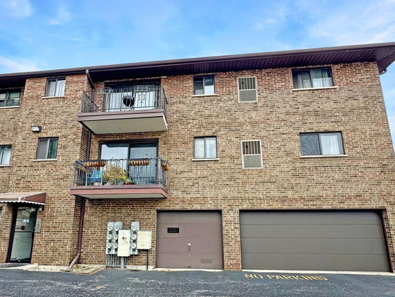 Front view of a three-story brick building with balconies and garages.