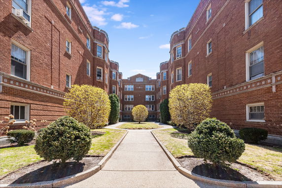 Front view of a brick multi-story building with a walkway and shrubs.