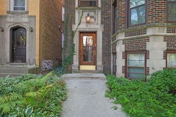 Front view of a brick building entrance with a wooden door and decorative arch.