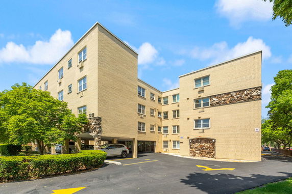 Front view of a multi-story apartment building with brick facade and parking area.