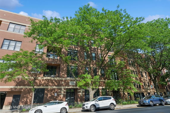 Front view of a multi-story brick building with large windows and trees in front.