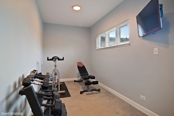 Small fitness room with exercise equipment including a bench, weights, and a stationary bike.