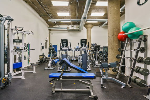 Interior view of a gym with exercise equipment including treadmills, weight benches, and free weights.