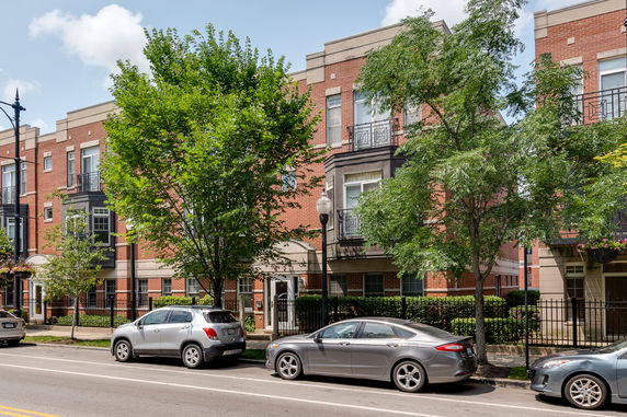 Front view of a multi-story brick building with balconies and several parked cars.