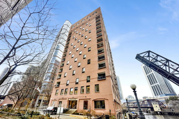 View of a multi-story building with numerous windows and balconies, adjacent to a bridge and waterway.