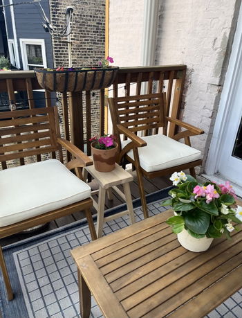 View of a small balcony area with wooden chairs and table, decorated with potted flowers and outdoor string lights.
